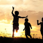 Children running on meadow at sunset